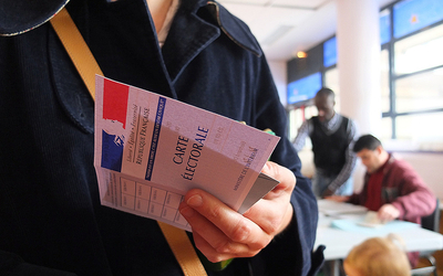 Votant dans un bureau de vote, carte électorale à la main