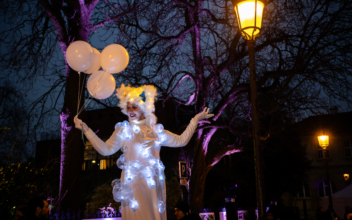 Artiste circacienne montée sur échasses avec des ballons blancs et une guirlande de lumières