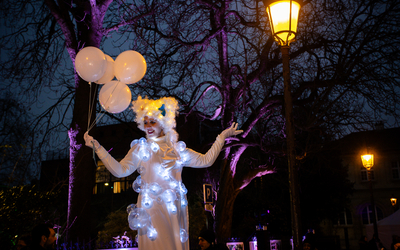 Artiste circacienne montée sur échasses avec des ballons blancs et une guirlande de lumières