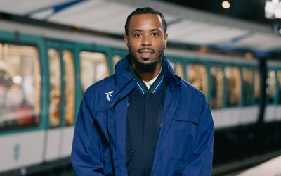 Portrait d'un homme souriant, habillé dans une tenue d'agent de RATP. En arrière plan, on voit un métro.