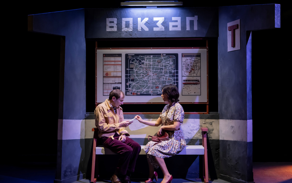 Sur une scène de théâtre, un couple assis sur un banc