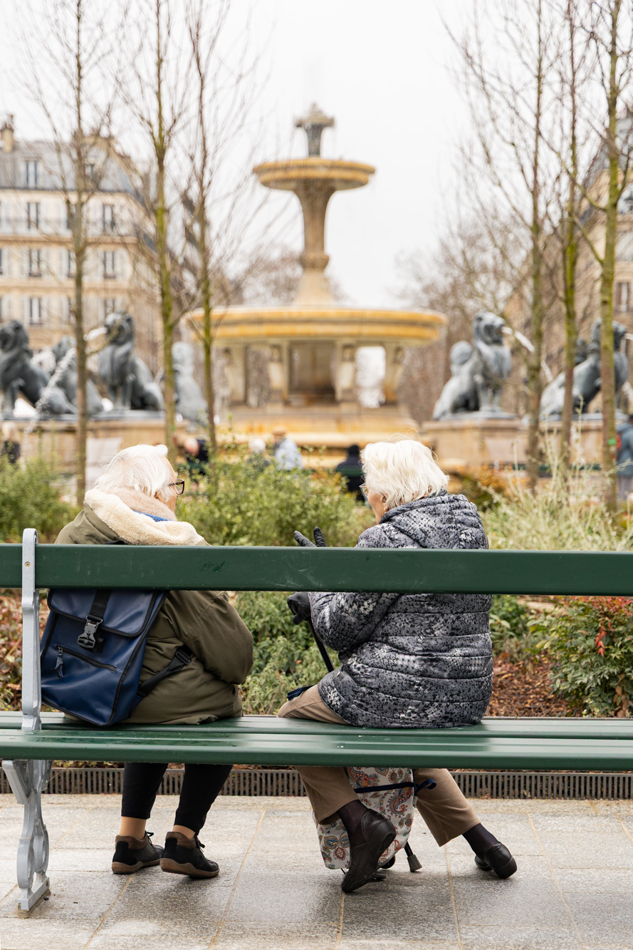 Deux femmes discutent sur un banc devant la fontaine aux lions de la place Félix Eboué