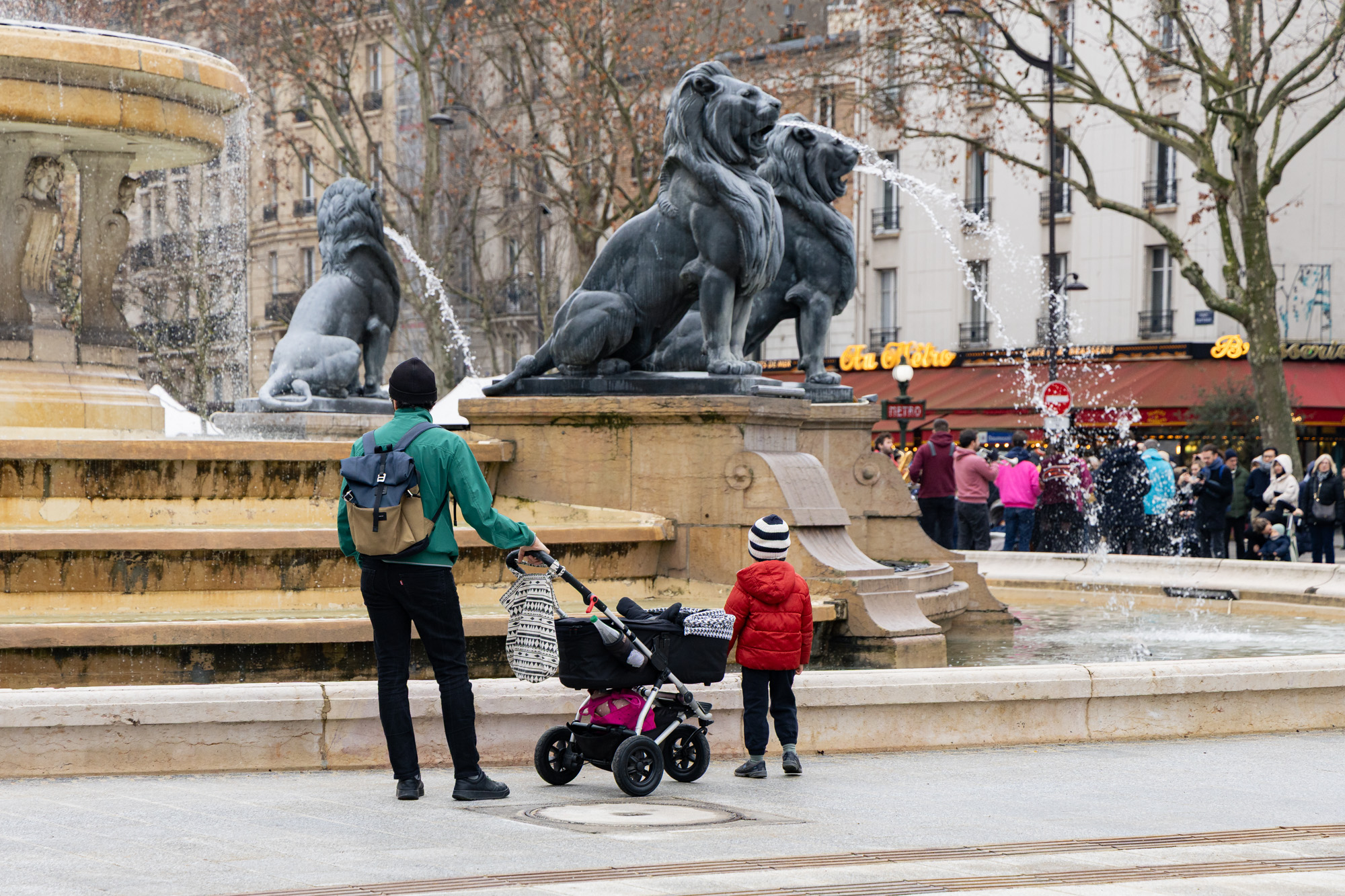 Une personne et un enfant regardent les fontaines de la place Félix Eboué.