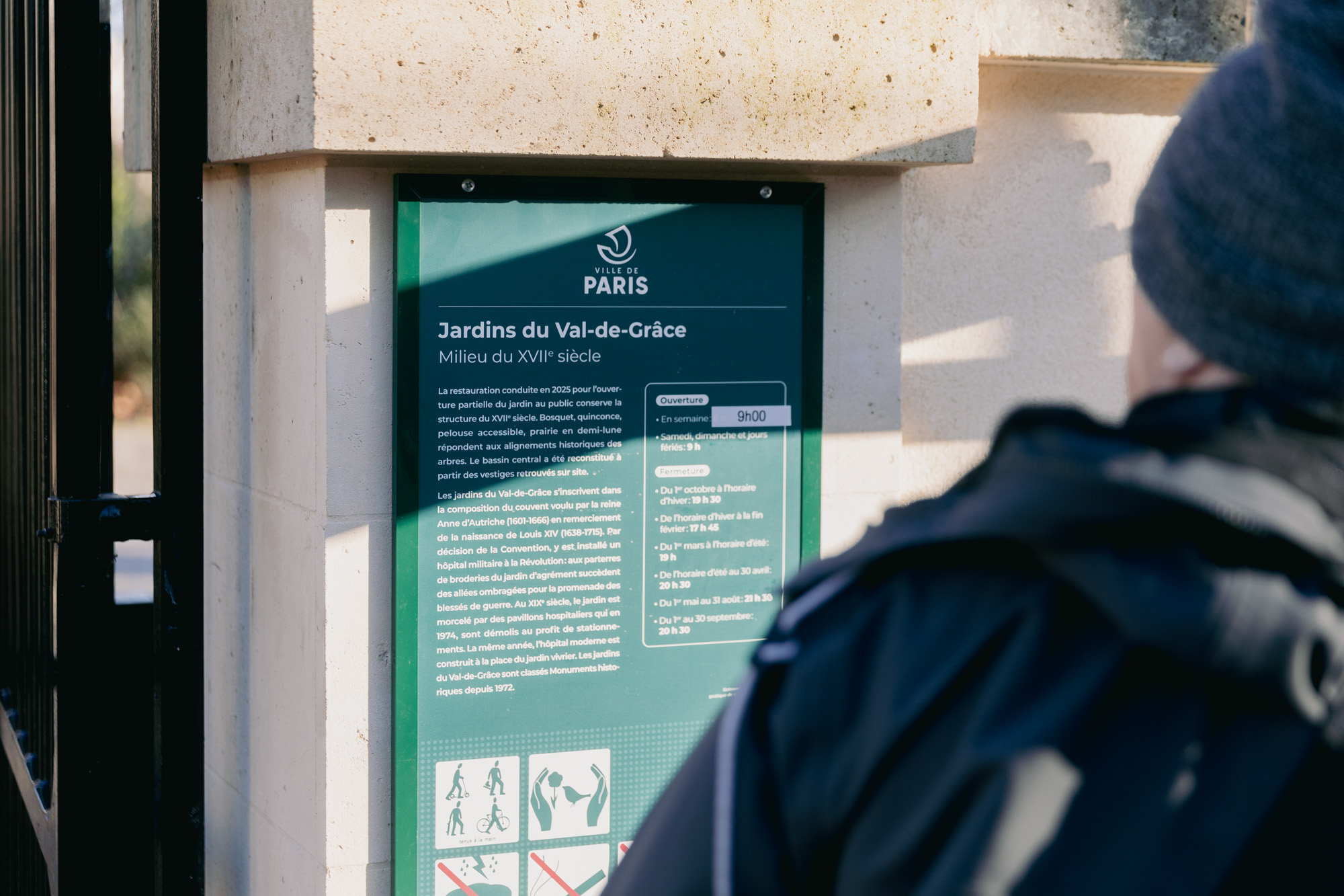 Une personne lit la plaque historique à l'entrée des jardins du Val-de-Grâce, 5e.