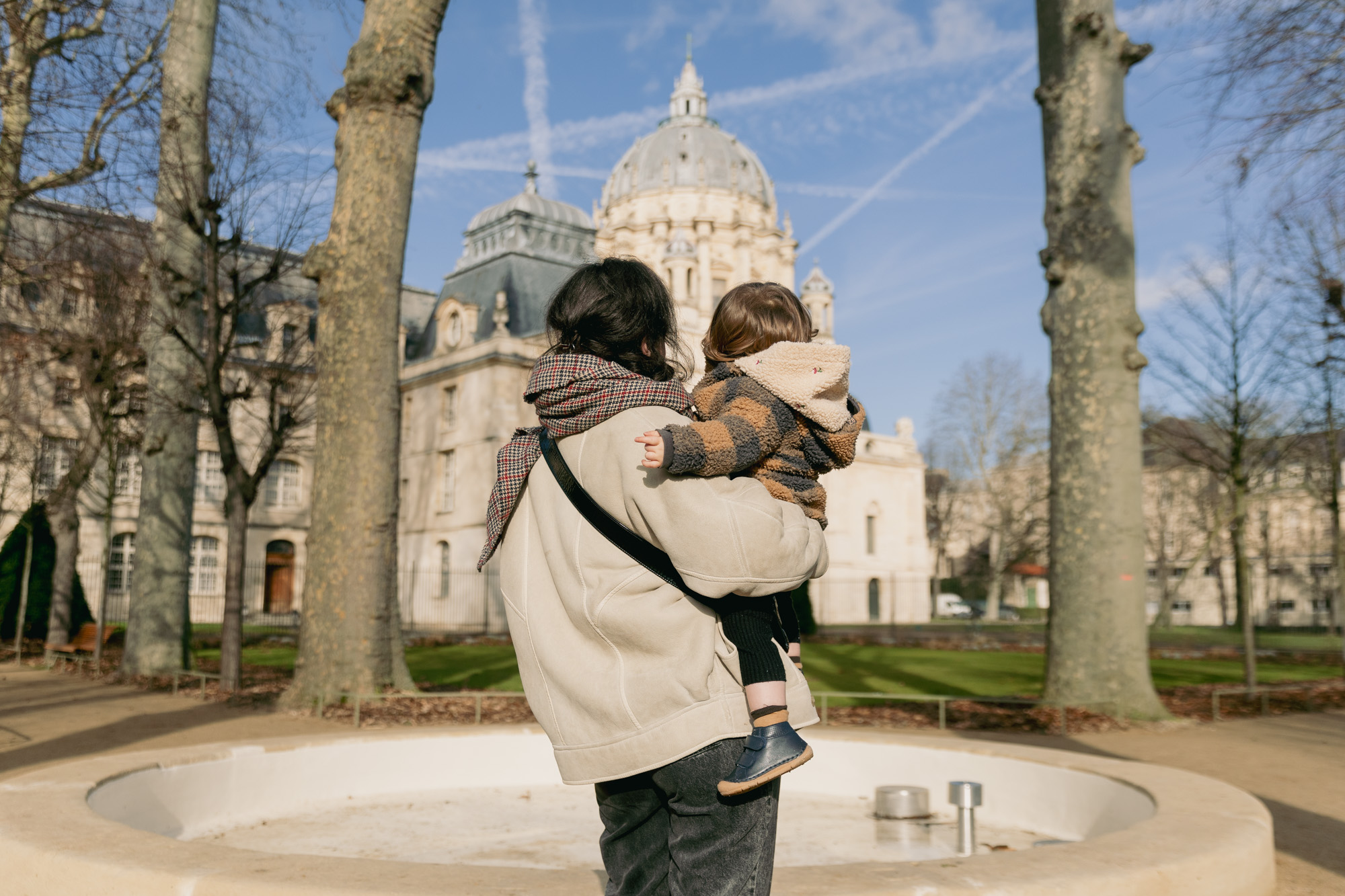 Une personne avec un enfant dans les bras dans les jardins du Val-de-Grâce, 5e.