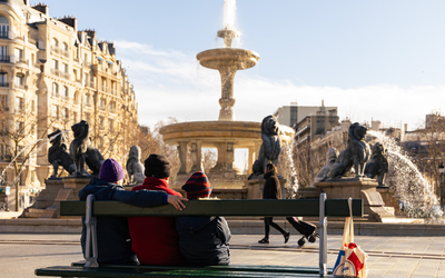 Des personnes installées sur des bancs devant la place Félix Eboué réaménagée, sous le soleil. 