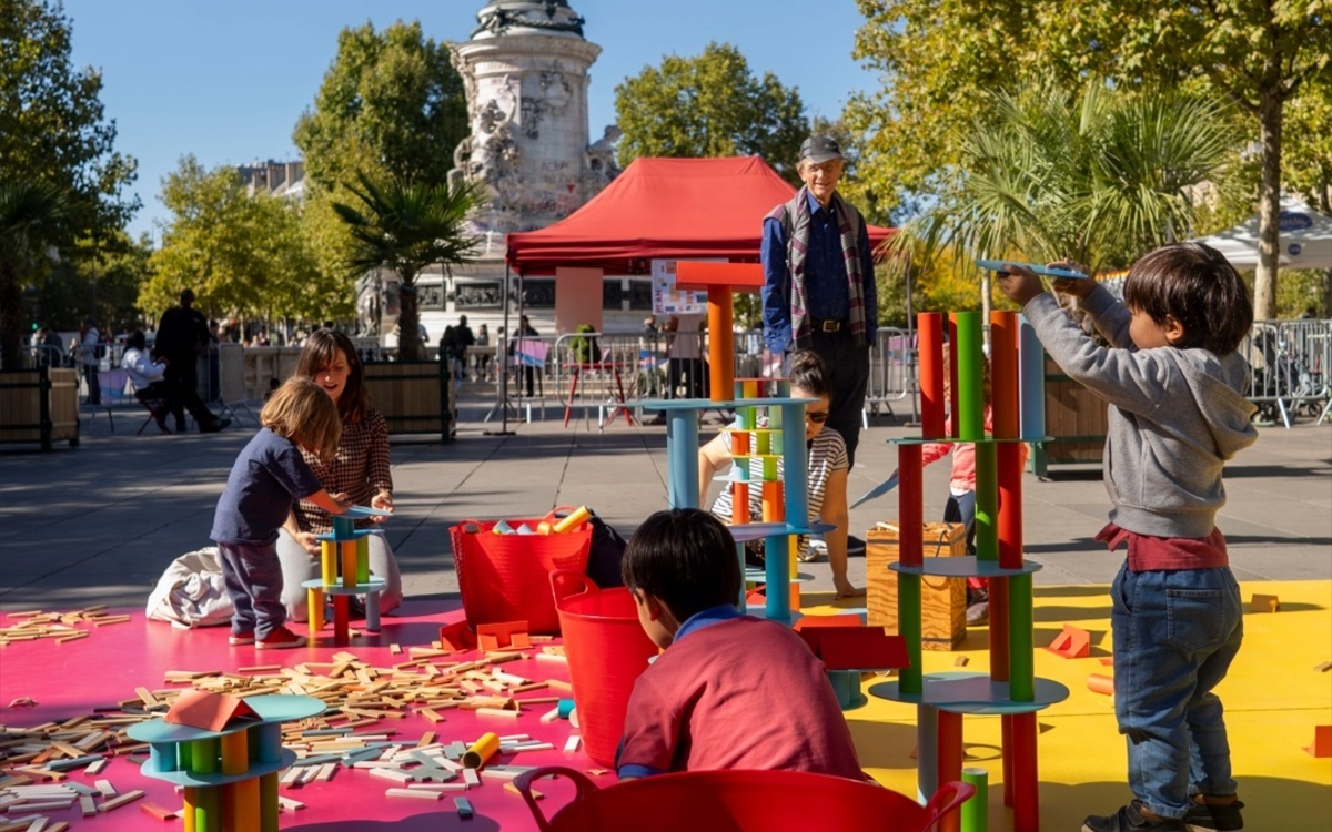 Petits enfants jouant à des jeux de construction sur un espace organisé tout exprès, place de la République à Paris, avec la statue de la République en arrière-plan.
