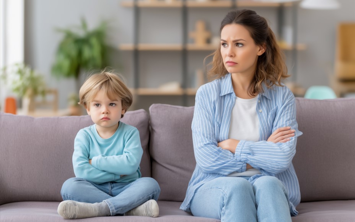 Un enfant et sa maman sont assis sur canapé avec les bras croisés. Ils regardent tous les deux vers deux différentes direction. Ils ont l'air d'être en colère
