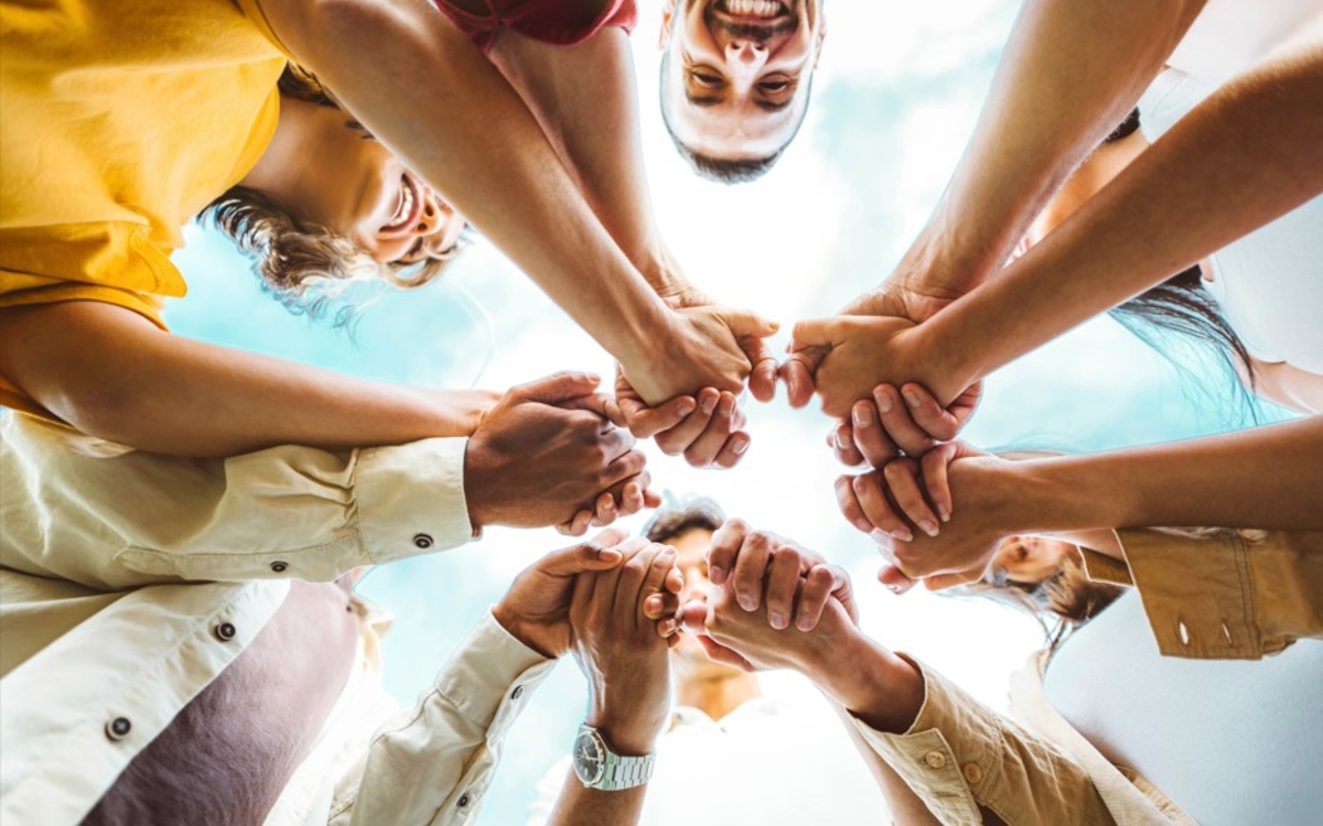Groupe de personnes qui se tiennent la main. Ils sont en cercle et ils réunissent leur main au centre du cercle.