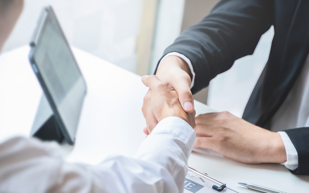 Deux hommes se serrent la main lors d'un entretien d'embauche. L'un porte une chemise et l'autre porte un costume.