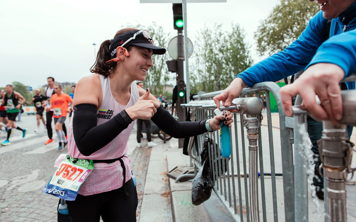 Une marathonienne remplit sa flasque d'eau tout en levant le pouce à destination du photographe.