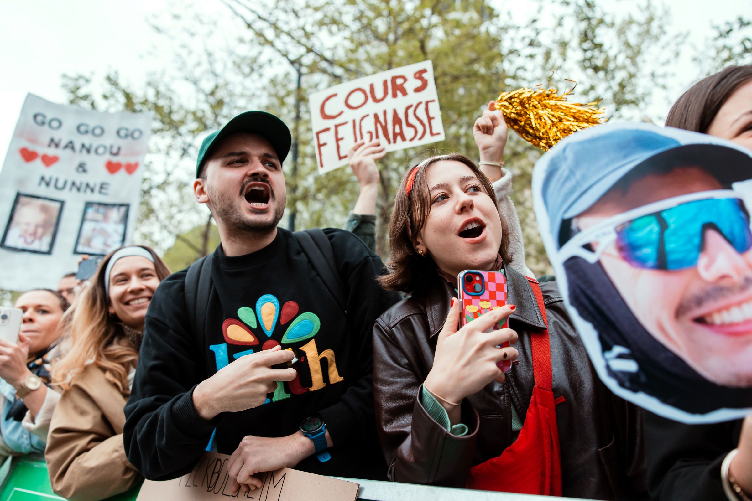 Un jeune homme et une jeune femme encouragent bruyamment des coureurs. A l'arrière plan, une pancarte "Cours feignasse". 