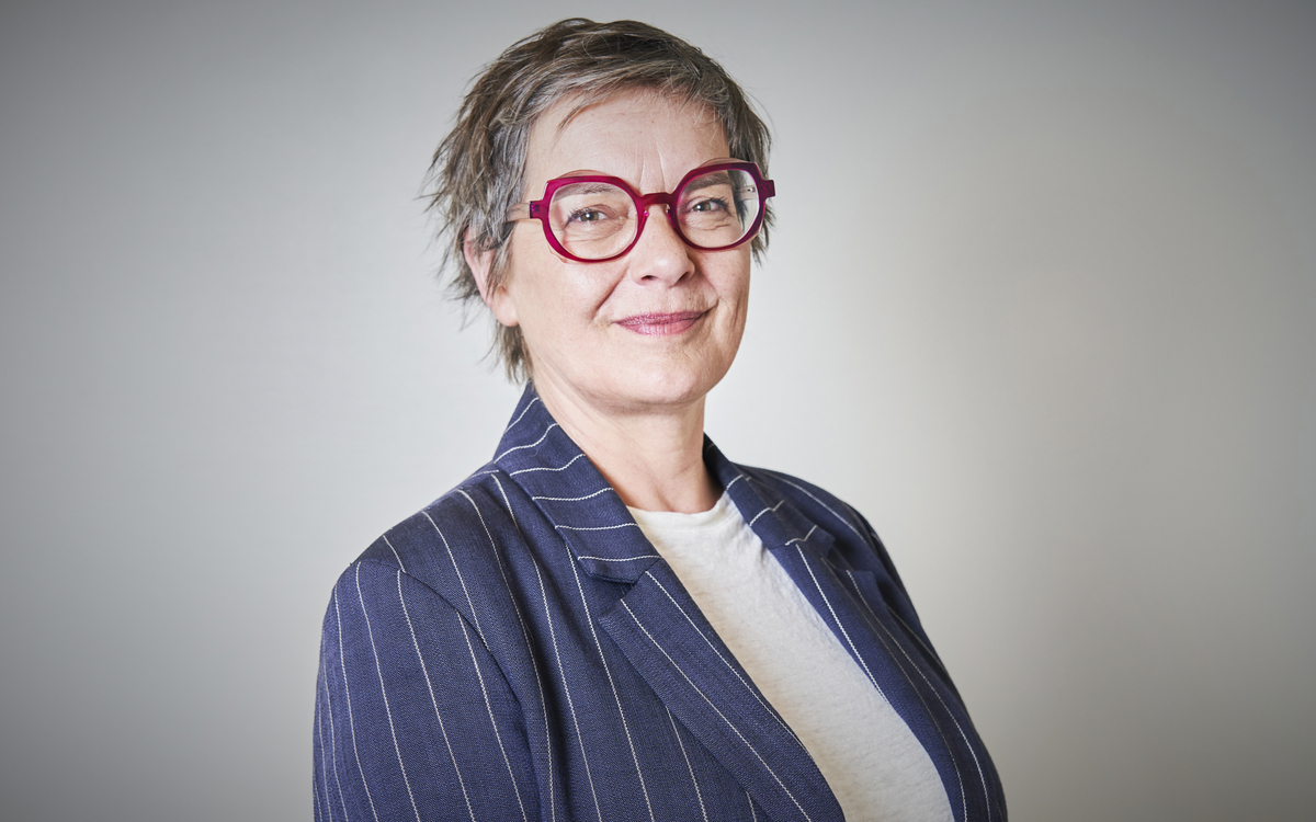 Portrait de Carine Petit avec lunettes rouges tee-shirt blanc et veste bleu marine rayures tennis