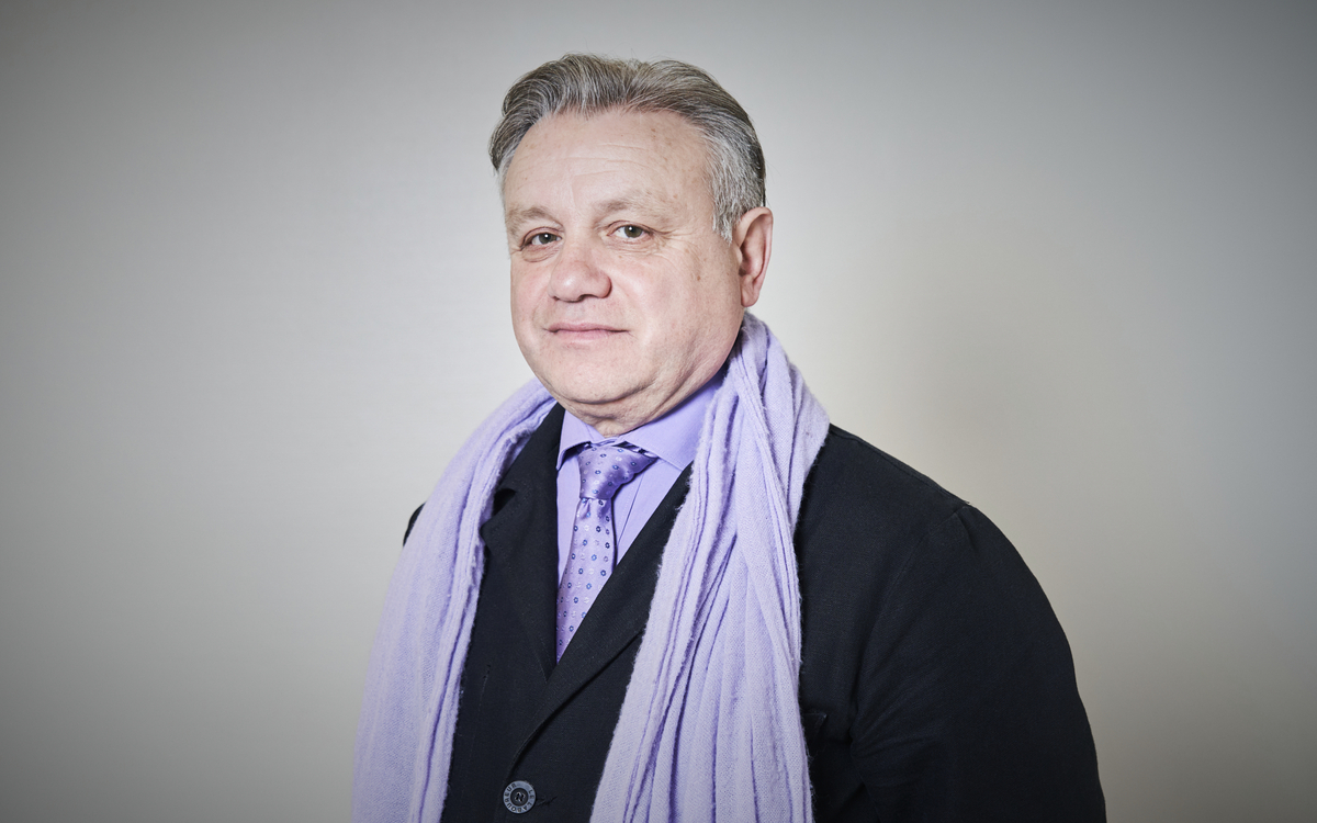 Portrait de Didier Antonelli portant une écharpe, une cravate et une chemise mauve avec une veste noire