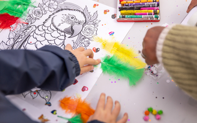 Des mains d'enfants travaillant sur un colage de plumes de couleurs vives