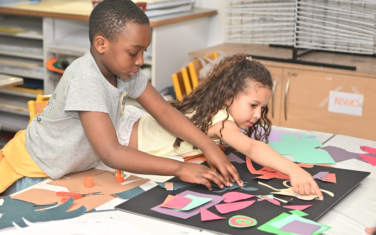 un petit garçon et une petite fille en train de coller des formes de toutes les couleurs sur leur grande feuille noire