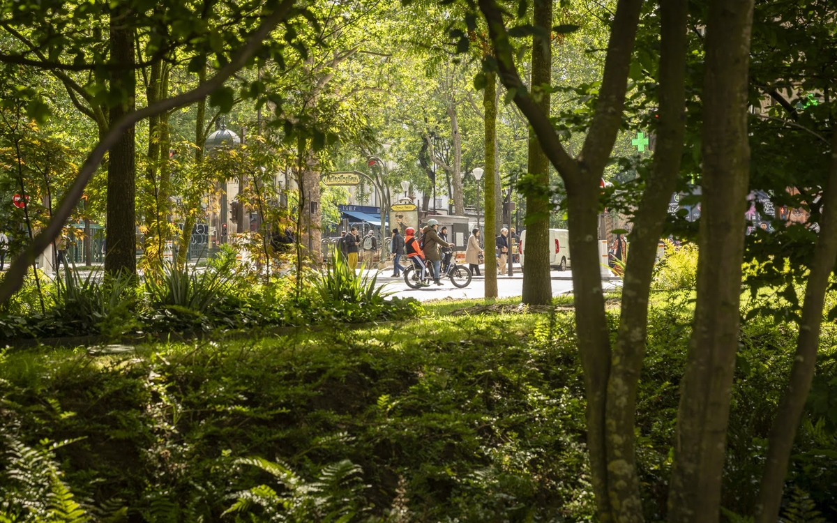Photo prise depuis les nouveaux espaces végétalisés de la place du Colonel Fabien. On y voit une végétation dense avec en point de mire des cyclistes sur les nouveaux aménagements