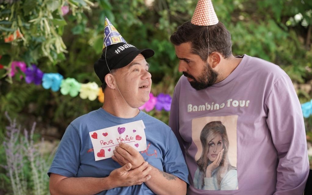 Photo d'Artus et d'un personne trisomique avec des chapeaux en papier et une guirlande en second plan