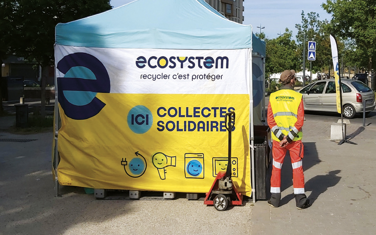 Photographie d'un bénévole qui pose de dos à côté d'un stand de collectes soldaires dans la rue