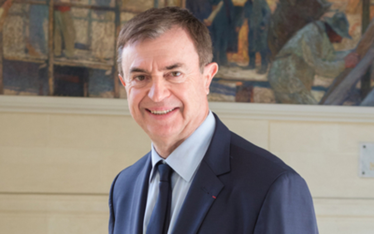 Photographie de Jean-Pierre Lecoq souriant en costume bleu marine avec une cravate de la même couleur et une chemise blanche