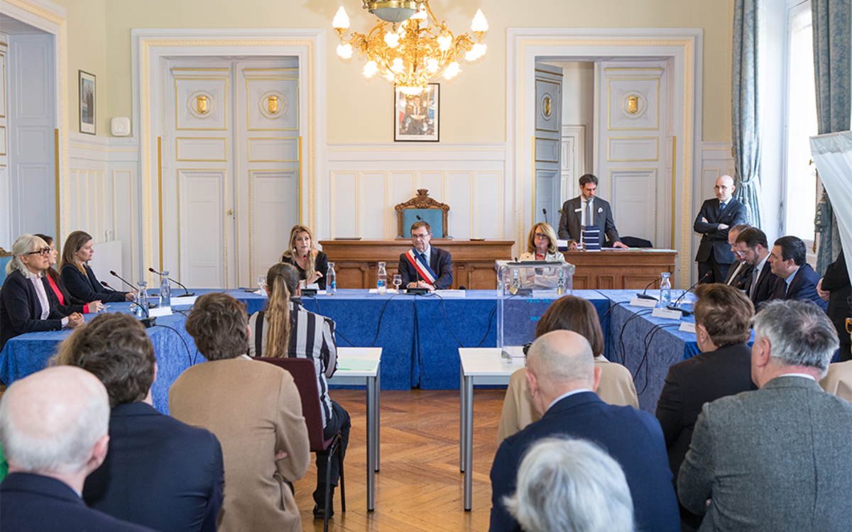 Photographie d'un Conseil d'Arrondissement montrant le Maire et ses élus assis à une table sous forme de U.