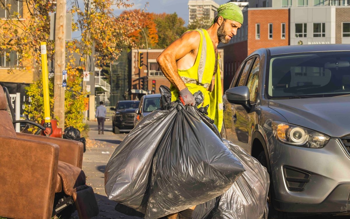 Un éboueur porte plusieurs sacs poubelles dans la rue