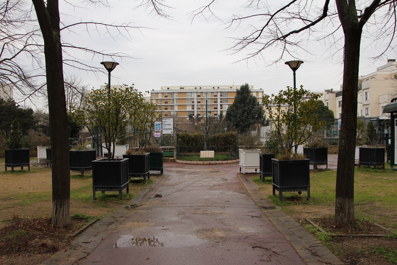 Le square Rajman avant travaux : sol minéral, petits arbres dans des pots, pas de visibilité sur la salle Olympe de Gouges