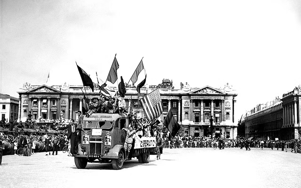 Photo en noir et blanc d'un camion circulant place de la Concorde avec des drapeaux français et américains