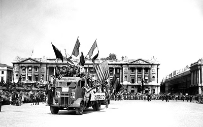 Photo en noir et blanc d'un camion circulant place de la Concorde avec des drapeaux français et américains