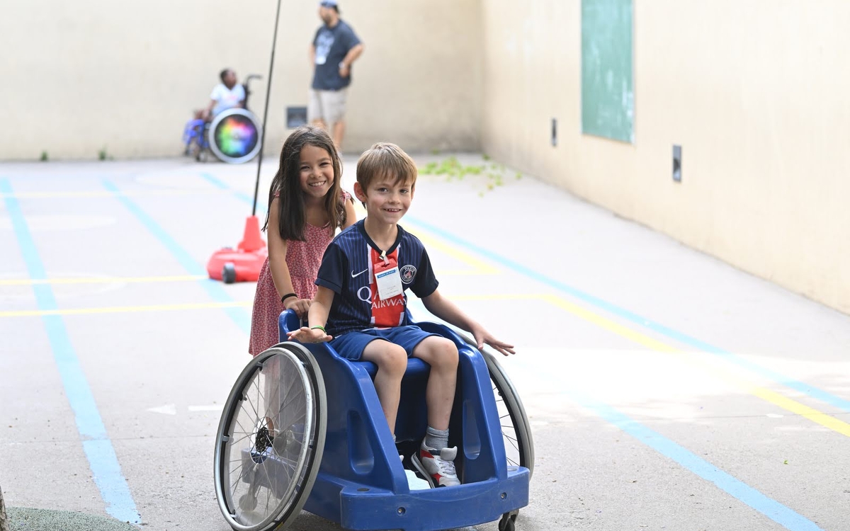 une petite fille pousse un petit garçon en fauteuil roulant dans une cour d'école