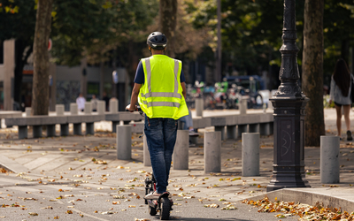 Une personne en trottinette électrique avec un casque et d'un gilet.
