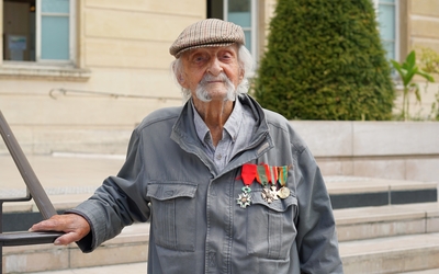 Jean posant devant la mairie du 14e casquette a carreaux et veste avec médailles