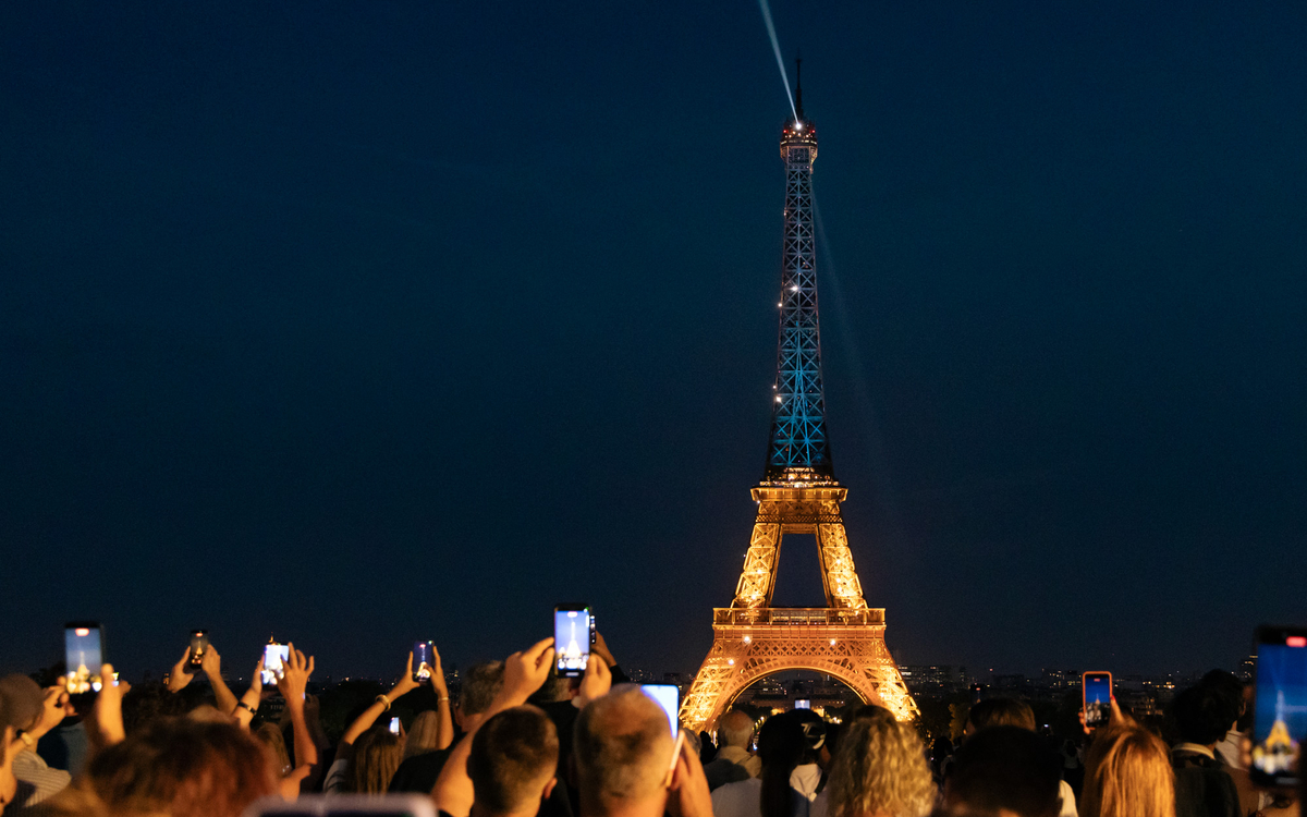 Des personnes photographient Tour Eiffel illuminée aux couleurs de l'Ukraine à l'occasion de la fête nationale ukrainienne.
