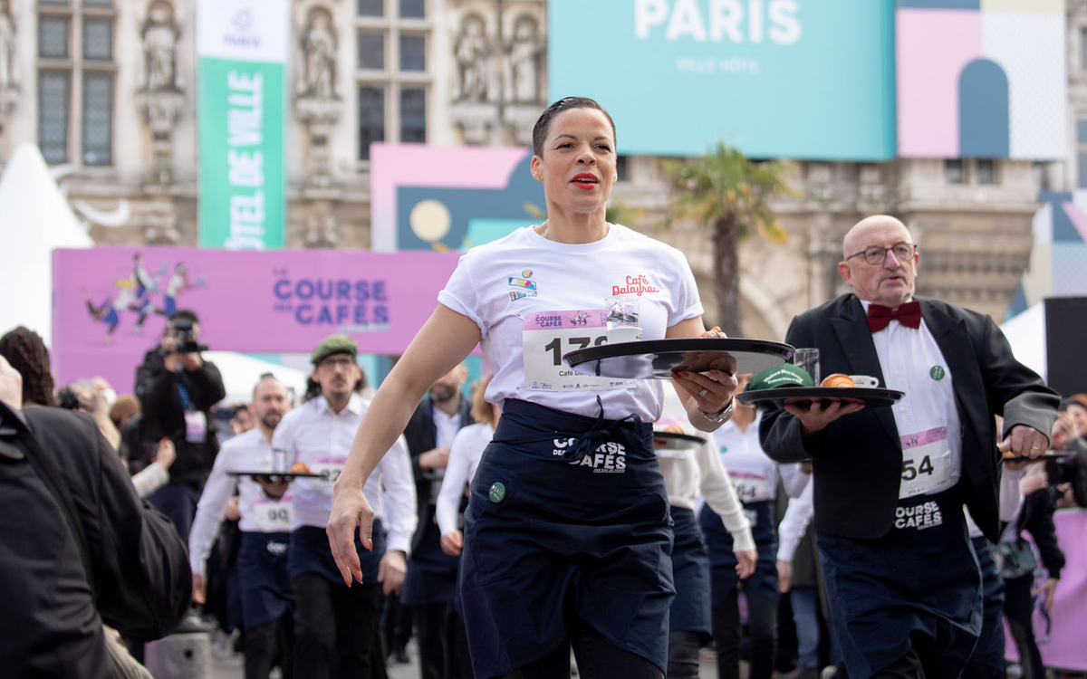 Des concurrents participent plateaux en main à la course des garçons de café devant l'Hôtel de Ville