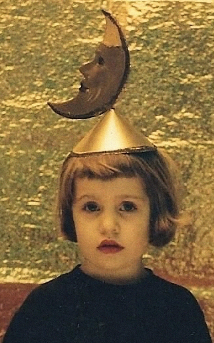 Une enfant (Léa Tissier, autrice du spectacle) porte un chapeau avec une lune en carton dessus. La lune a un visage. L'enfant est devant un fond doré.