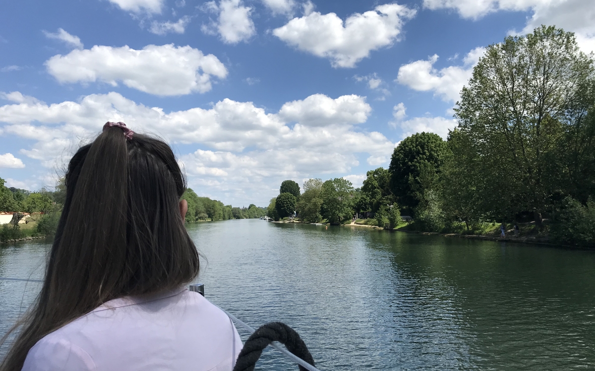 Une passgère de dos contemple l'eau de la Marne sur un bateau