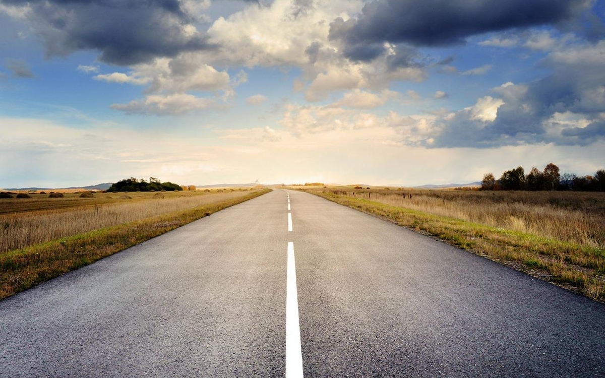 une route entourée de champs jusqu'à l'horizon, avec du ciel bleu et des nuages.
