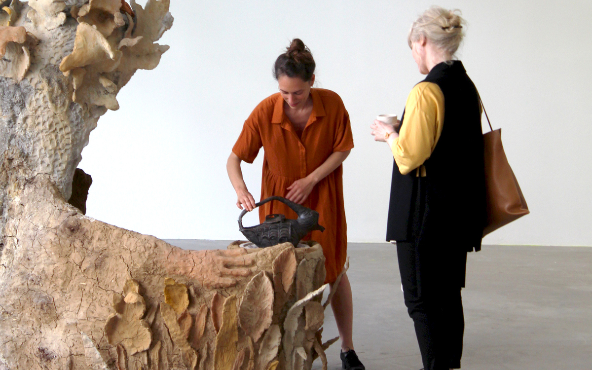 L'artiste Tiphaine Calmettes servant une tasse d'infusion à un visiteuse dans le cadre de son exposition