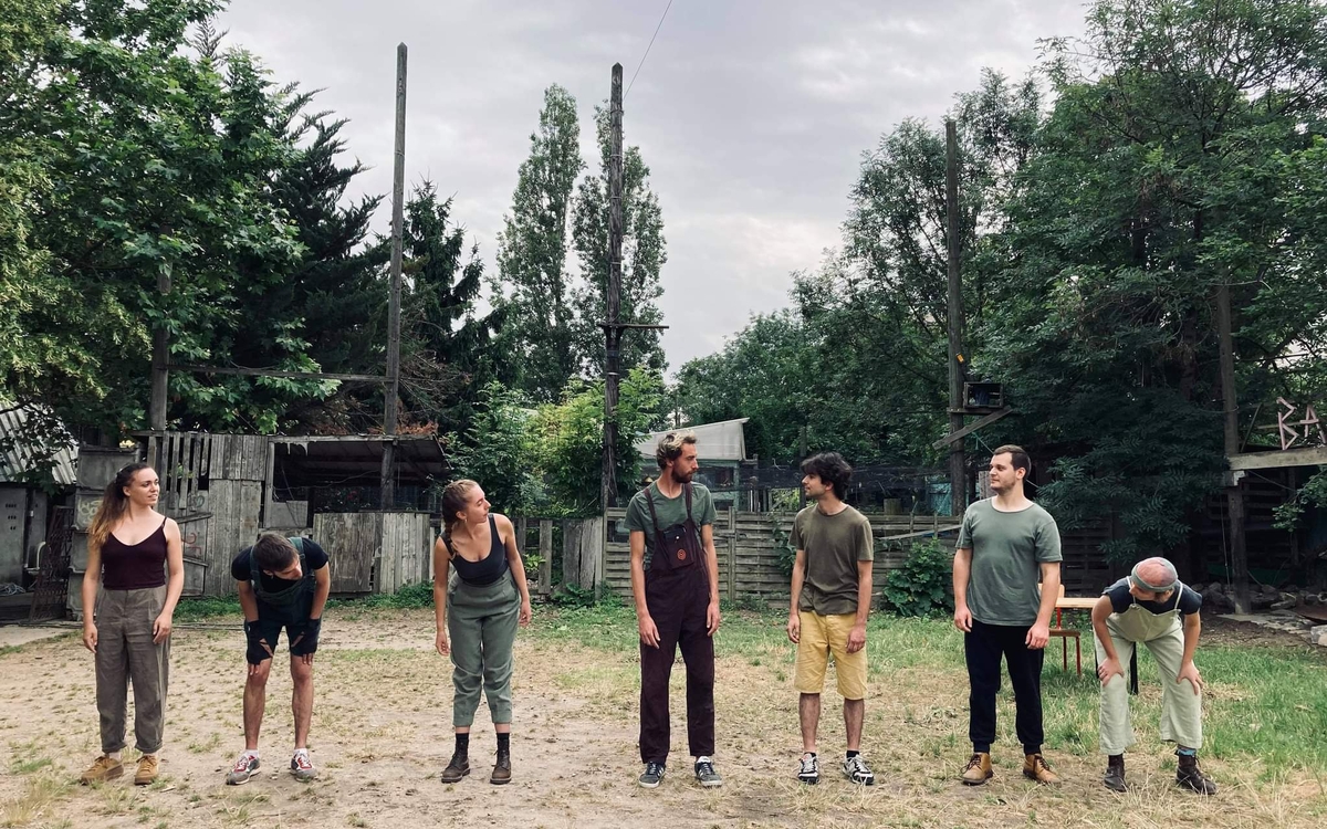 Sept personnes alignées devant une forêt. Elles se regardent entre elles