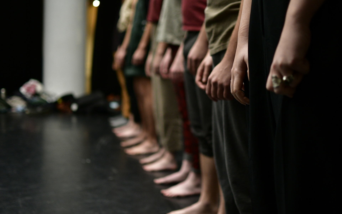 Des personnes alignées, prise de côté, on ne voit pas leur visage mais la file de leurs bras et de leurs pieds