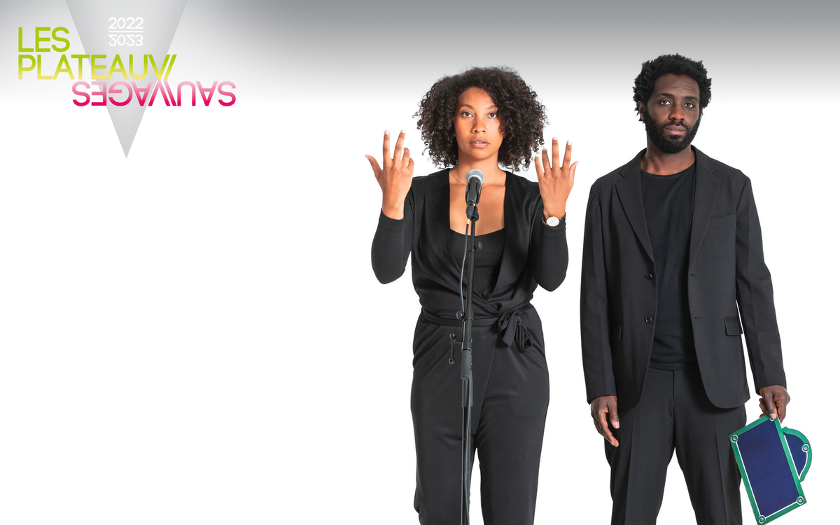 Un duo, femme et homme, habillés en noirs nous regardent. Elle est face à un micro et lèves les mains. Il tient un panneau parisien qui indique le nom des rues mais rien n'y est écrit.