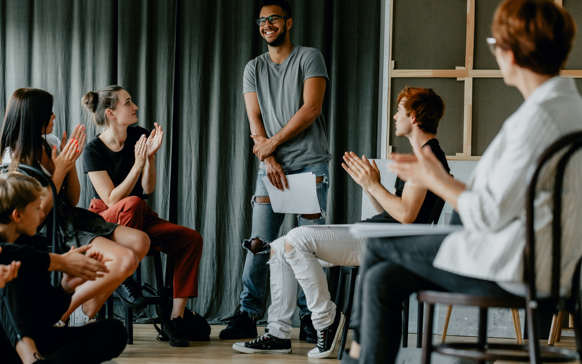 une personne est debout et les autres applaudissent. Elles applaudissent et regarde la personne debout.