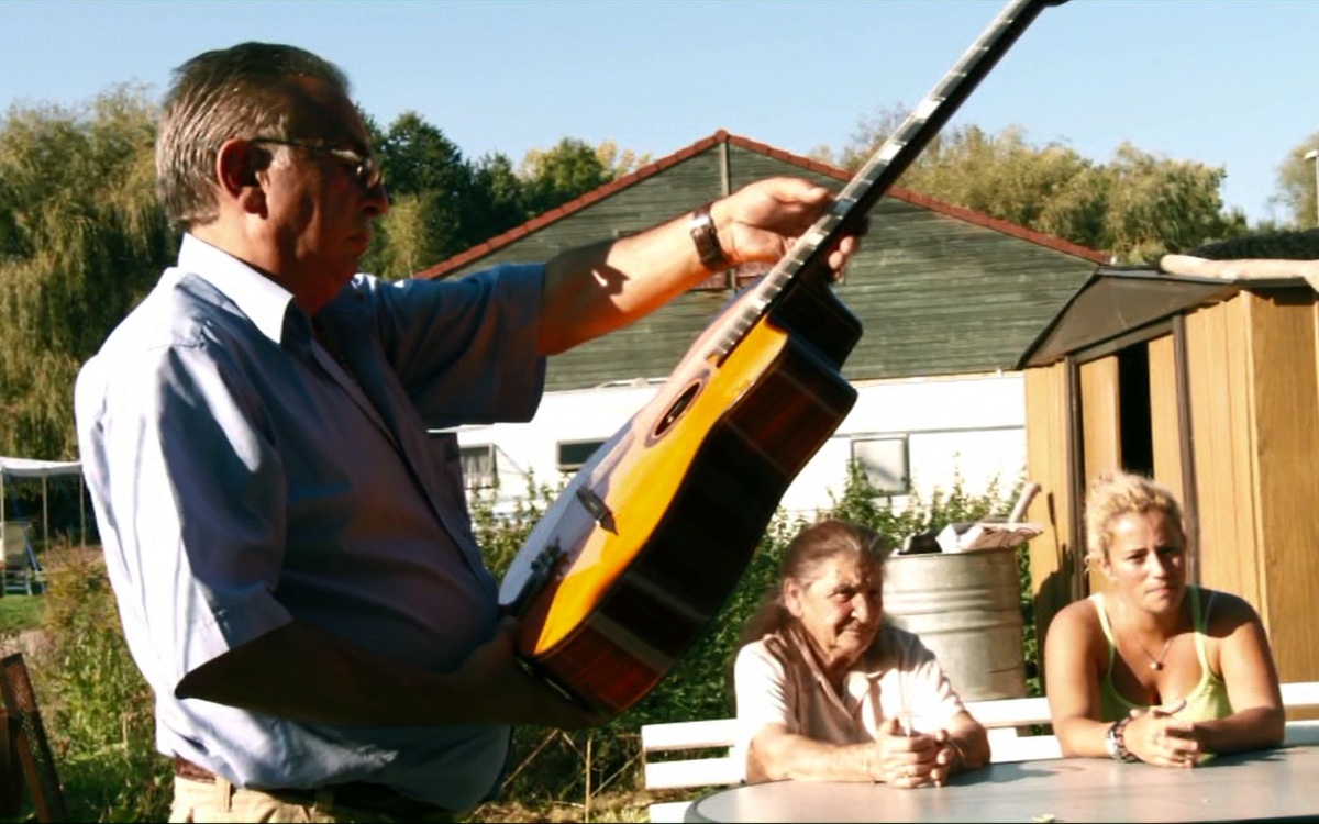 "Forbach Swing" de Marie Dumora - une homme debout en extérieur tient une guitare sèche, qu'il regarde attentivement.