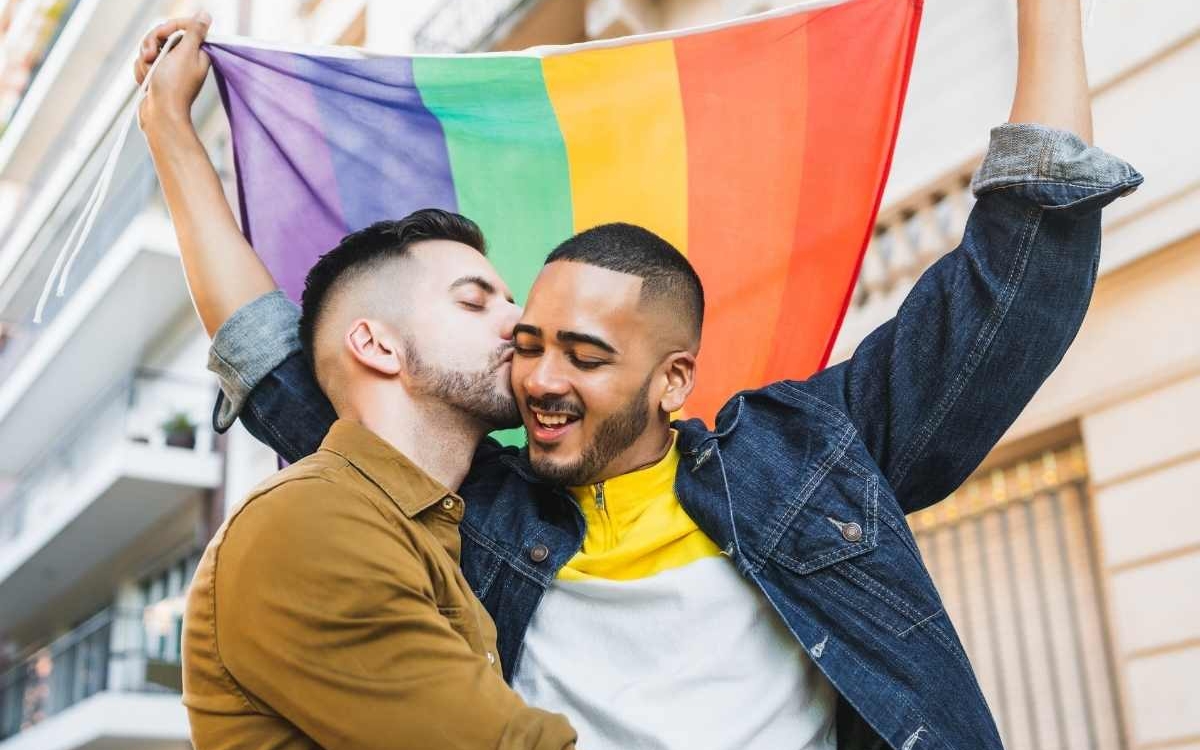 Deux hommes s'embrassent en brandissant un drapeau aux couleurs arc en ciel