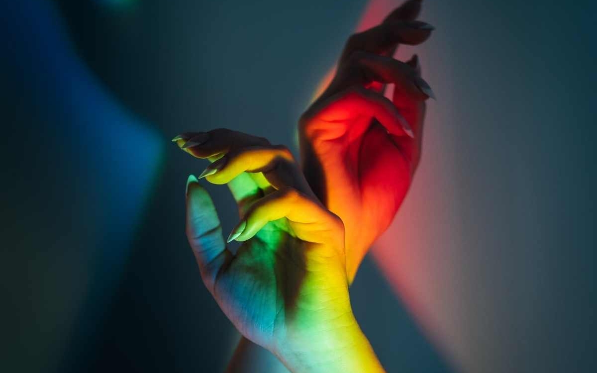 Des mains levées sous une lumière arc en ciel