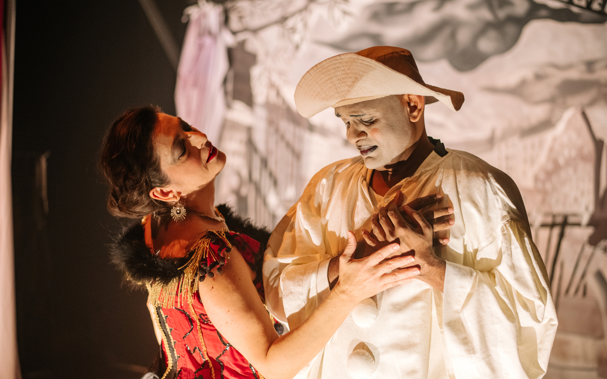 Mime le regard vers le bas, comme attristé, joint ses mains au coeur, une femme vêtue de rouge à côté de lui pose sa main sur les deux mains du mime.