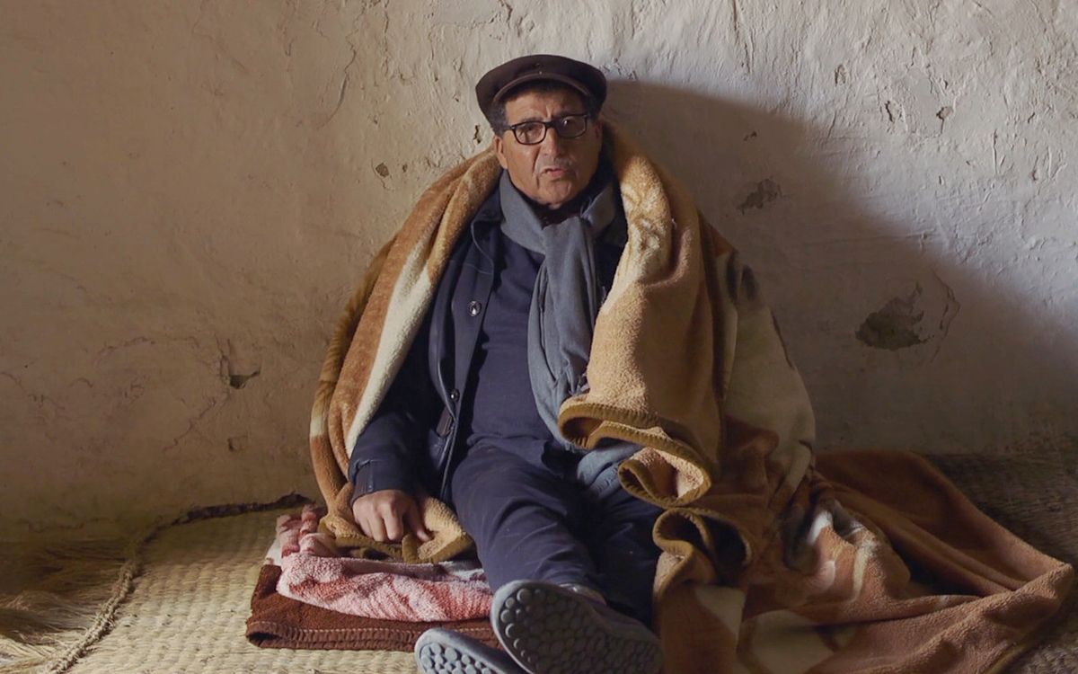 un homme assis sur le sol, à l'intérieur d'une maison en Algérie, adossé au mur. Extrait du film À Mansourah tu nous as séparés de Dorothée-Myriam Kellou. Projection aux Ateliers Varan à Paris.