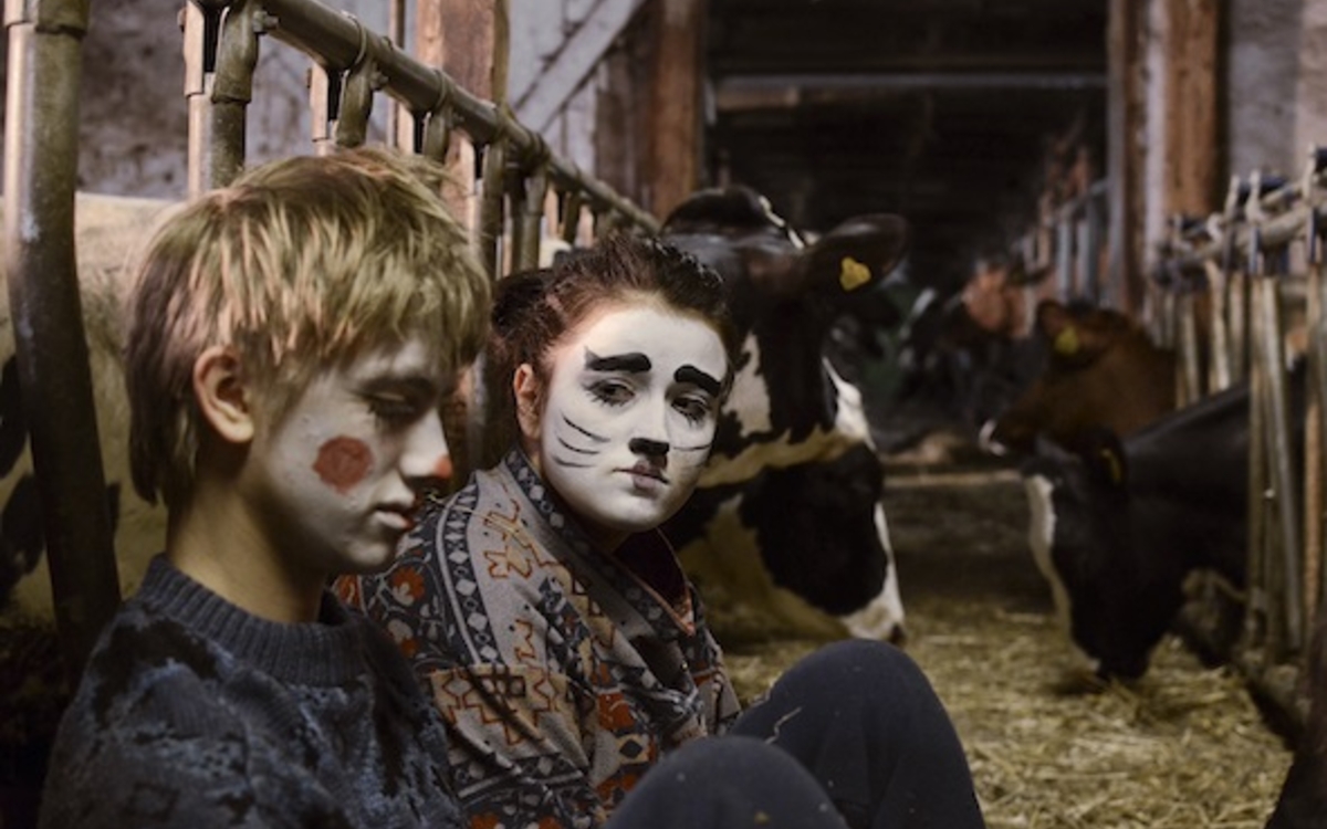 Deux enfants maquillés en clown et chat, sont assis près d'un enclot à vaches