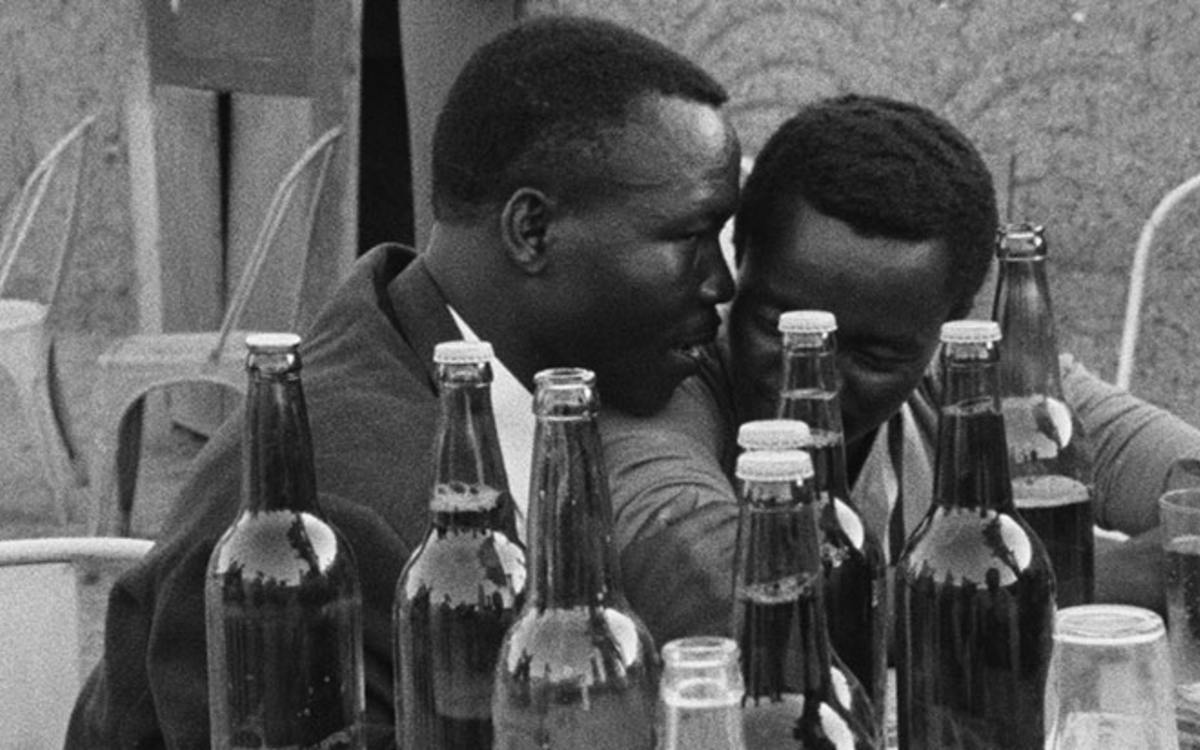 Deux hommes noirs discutent à table, l'un parle à l'oreille de l'autre. Extrait du film de Oumarou Ganda, "Cabascabo". Les Dimanches de Varan Ateliers Varan