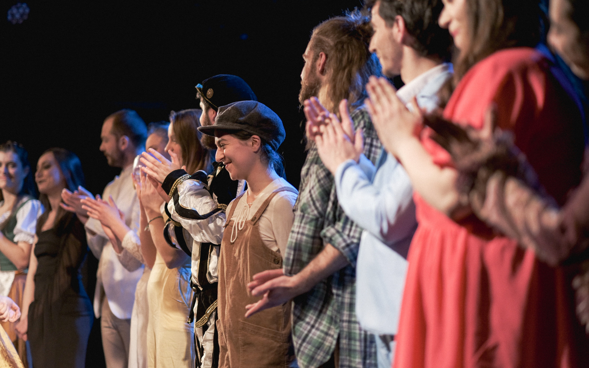 Troupe sur scène, lors du salut face au public, à la fin du spectacle. Ils applaudissent avec le public, le sourire aux lèvres.
